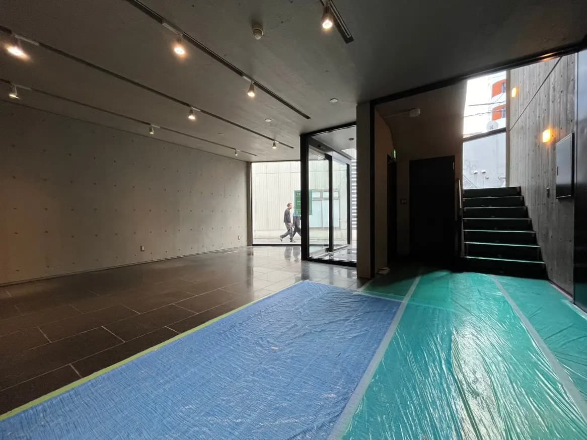 現代的な建築スタイルのエントランスホール、コンクリート壁面、スポットライト照明、床にブルーシートが敷かれた改装中のスペース