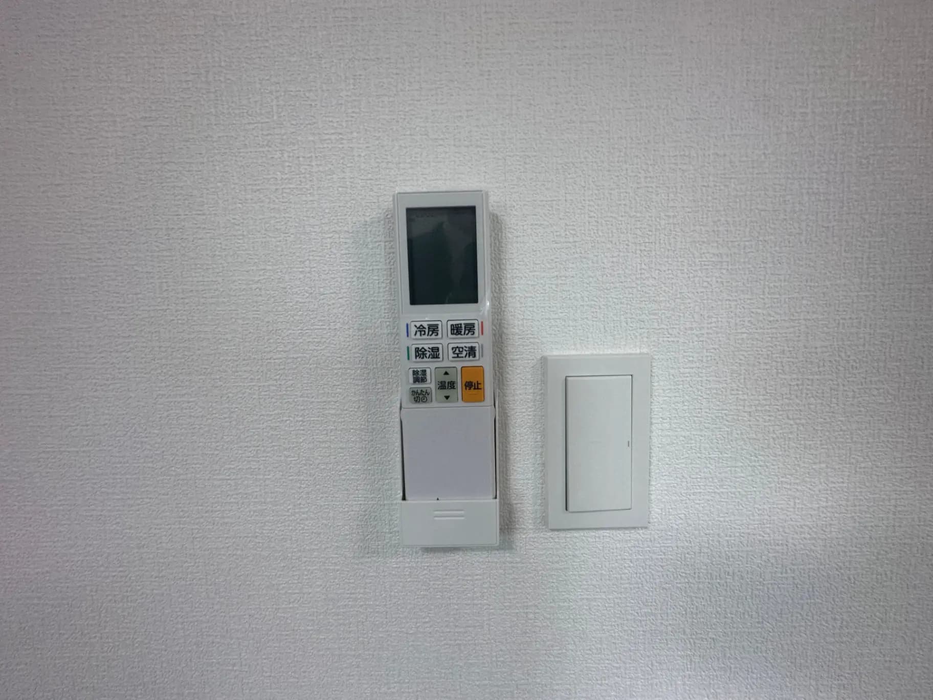 室内のエアコンリモコンとスイッチが壁に設置されている、ミニマルなインテリアデザイン