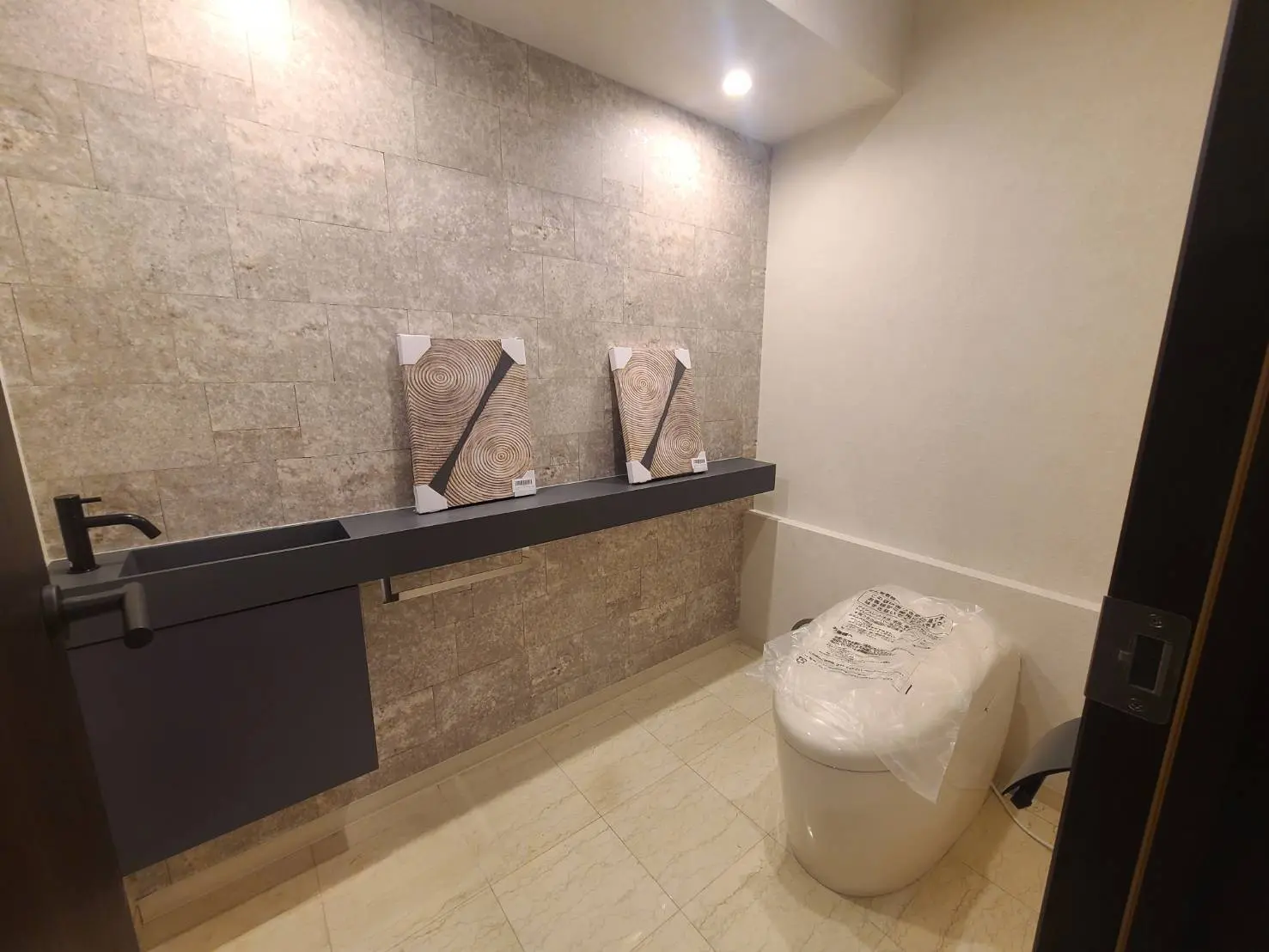 モダンなデザインのトイレルーム、壁面デザインタイル、黒い手洗いカウンターと木目調アクセント