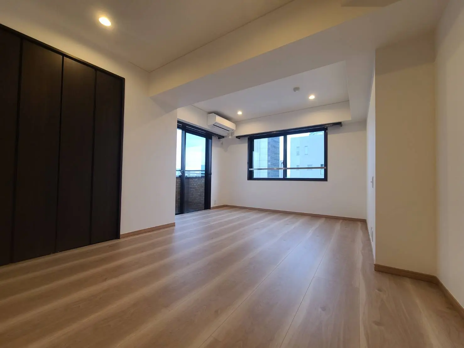 シンプルなデザインの空の部屋、木目調フローリング、大きな窓と充分な照明、内蔵クローゼット付き