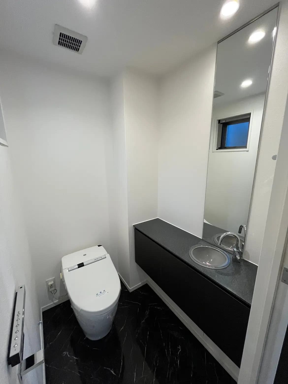 現代的なデザインのトイレルーム、黒の大理石調フロア、壁掛けタイプの洗面台、ウォシュレット付き便座