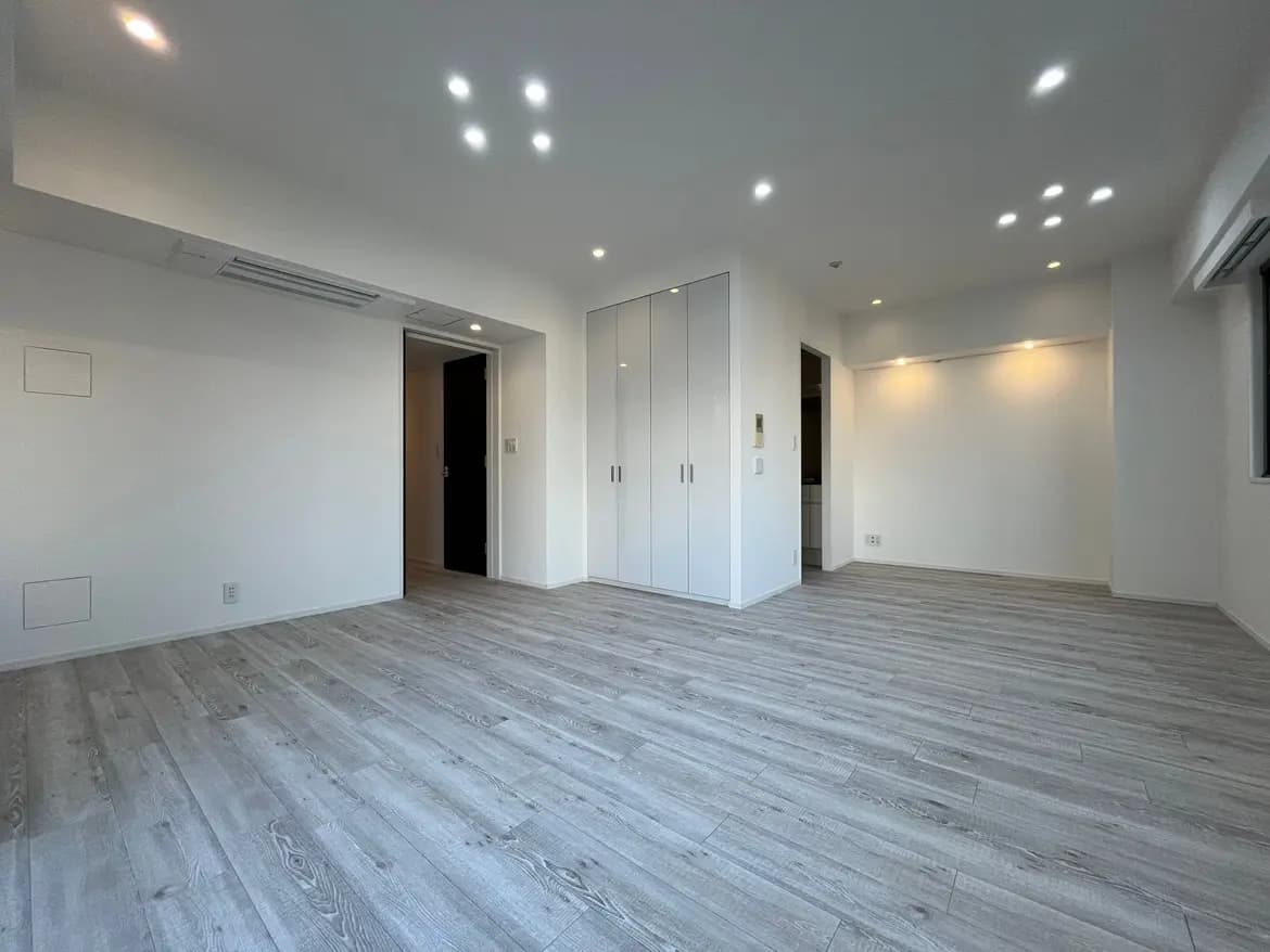 シンプルで洗練されたデザインの空の部屋、グレーの木目調フローリング、白い壁と内蔵クローゼット