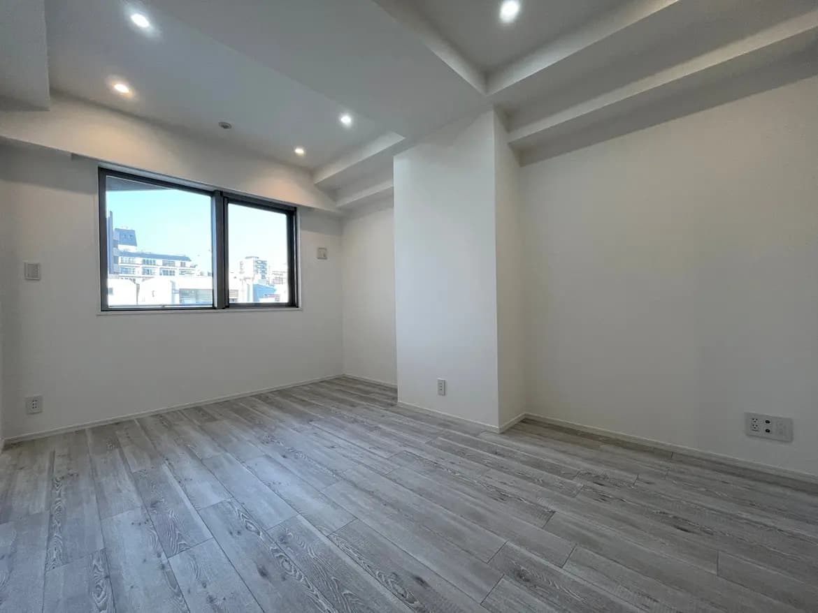 新築のモダンな空の部屋、灰色の木目調フローリング、白い壁と天井、都市の景観が見える大きな窓