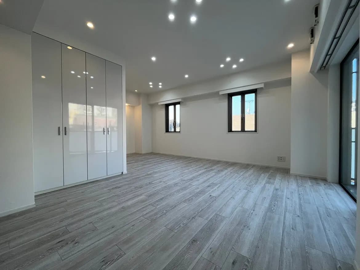 空間が広く明るいモダンな部屋、グレーの木目調フローリング、白い壁と大容量のクローゼット、ダウンライトの天井