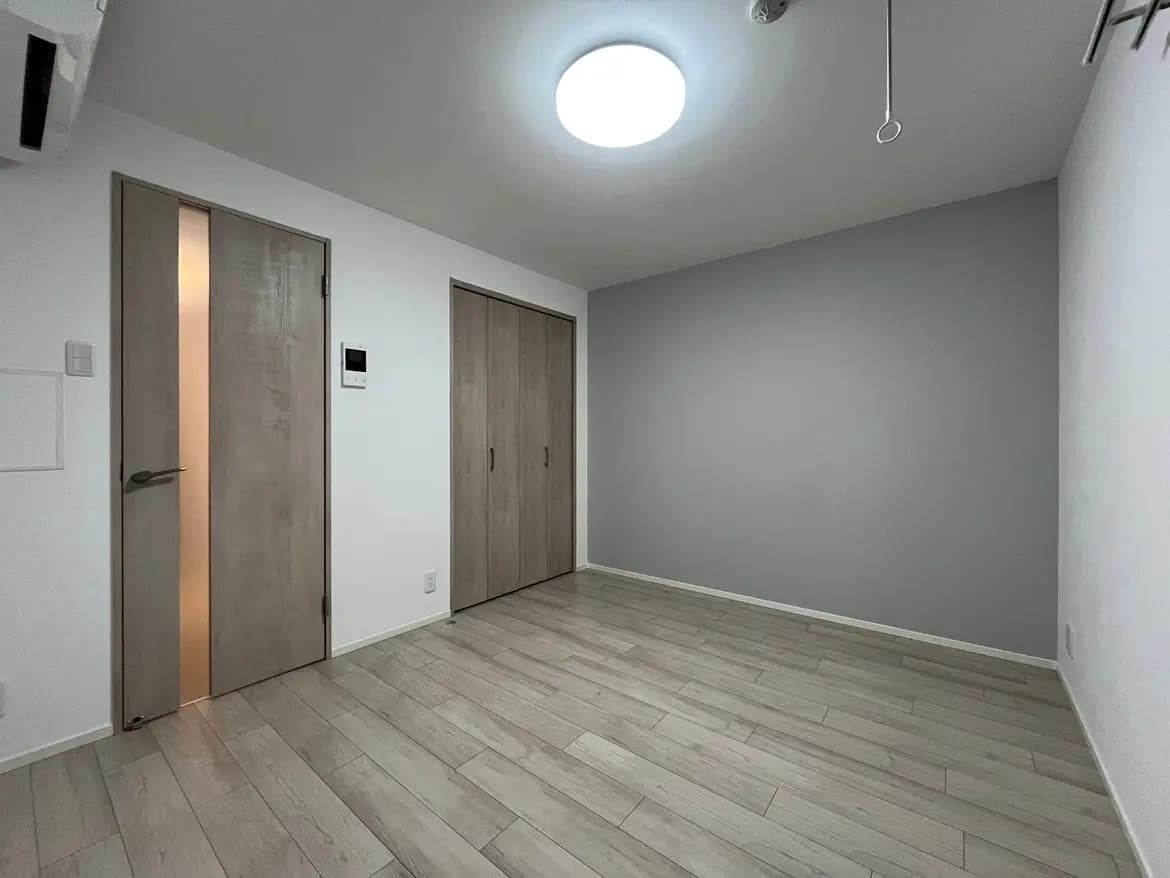 シンプルな内装の空の部屋、木目調のフローリング、灰色の壁、丸い天井照明
