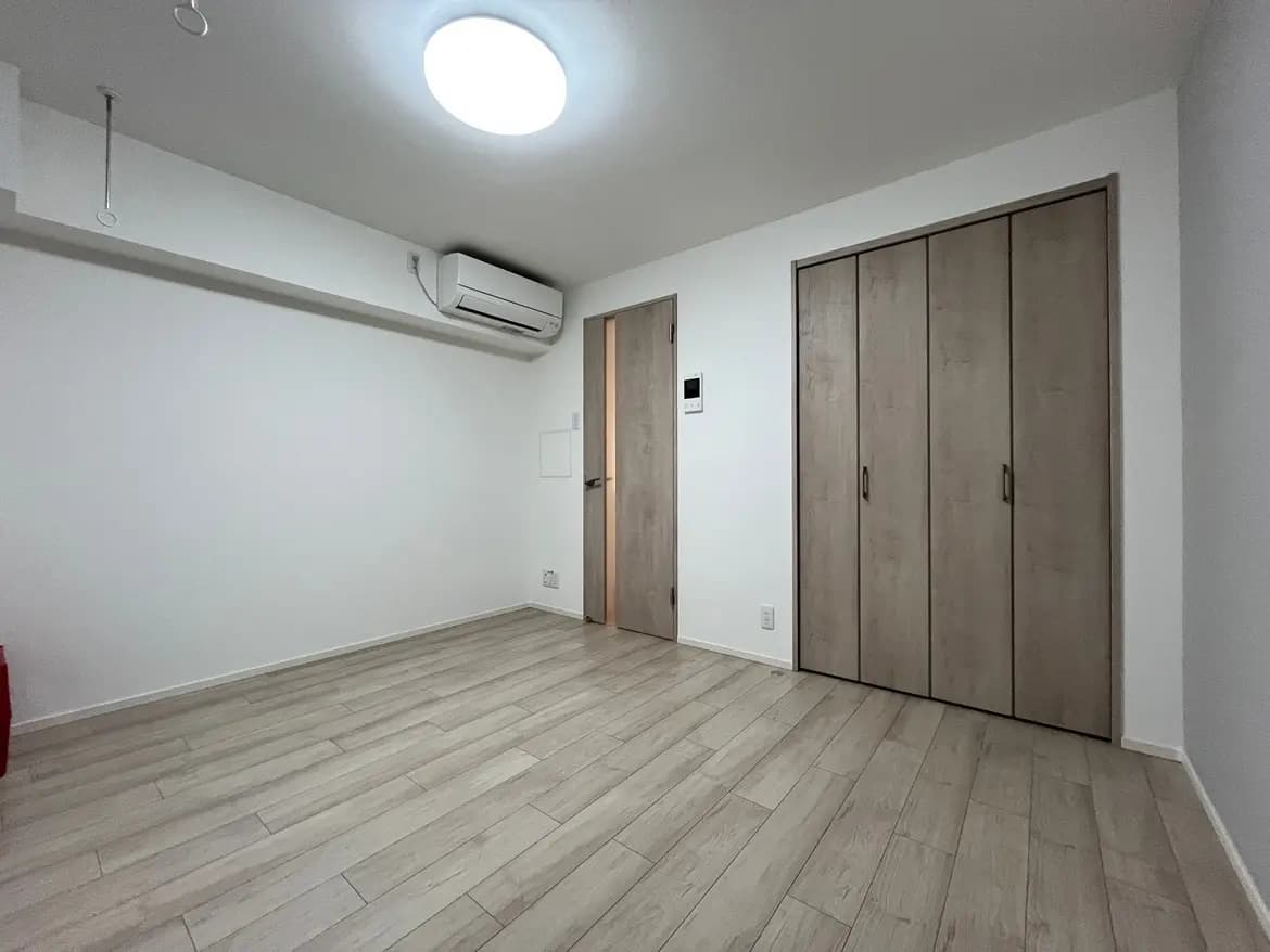 シンプルなデザインの空の部屋、エアコン付き、木目調フローリング、白い壁と建込みクローゼット