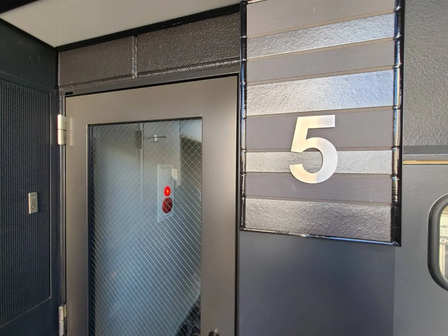 モダンなアパートのエントランスドア、表札に数字の5、格子ガラスと防犯カメラ