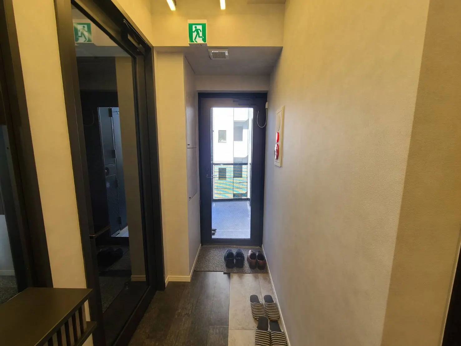 シンプルなデザインの玄関ホール、避難口標識とスリッパが置かれた室内