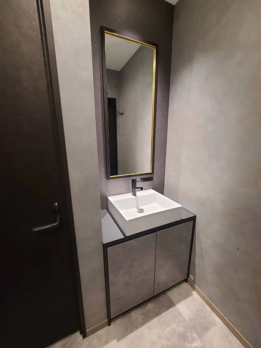 シンプルでモダンな洗面所、黒いフレームの鏡と灰色の壁、洗面台とキャビネット