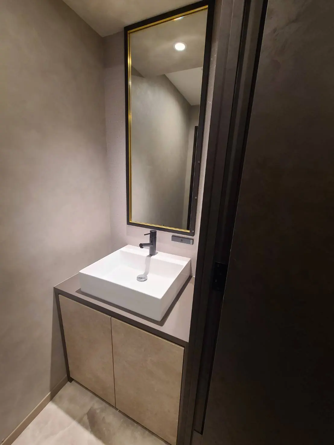 ミニマリストデザインの洗面所、ゴールドフレームのミラーとモダンな洗面台が特徴的なインテリア