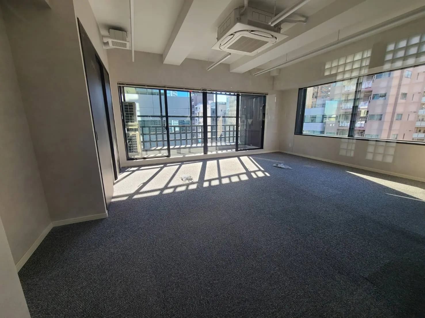 明るい日差しが差し込む空のオフィススペース、大きな窓とベランダ、都市の景色