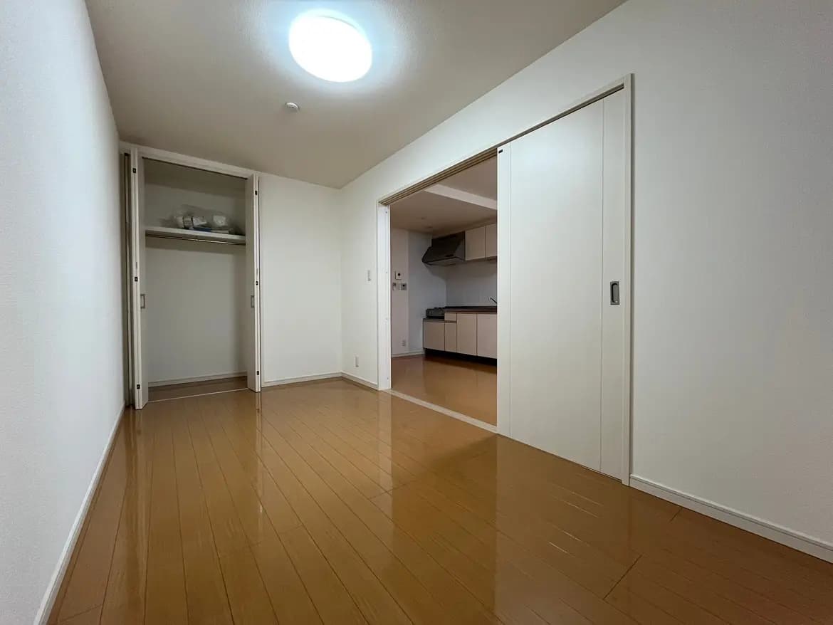 綺麗に整頓された空の部屋、木製フローリング、白い壁、開けた収納スペースと照明のあるモダンなインテリア