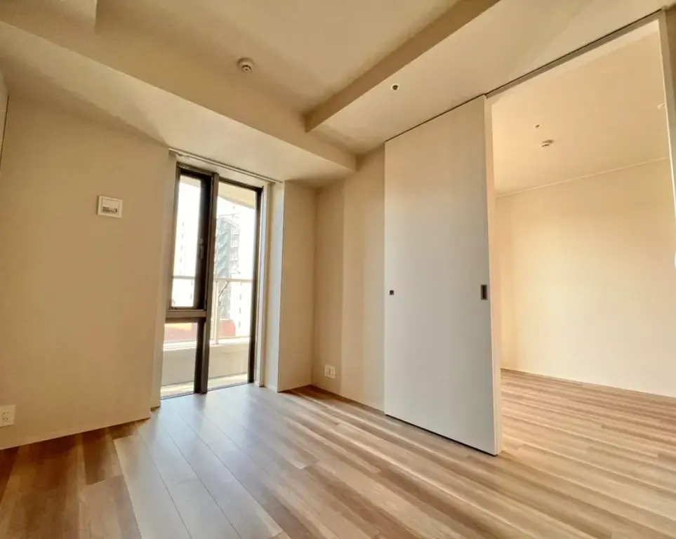 シンプルなデザインの明るい空間、木製フローリング、大きな窓とクローゼットがある新築マンションの部屋