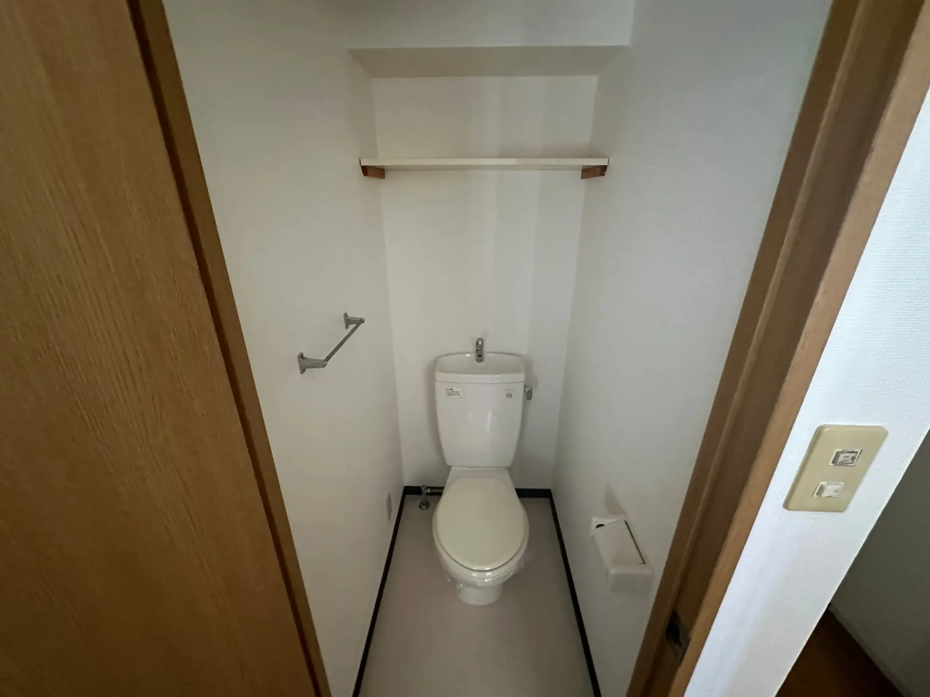 コンパクトなトイレルーム、白い壁と木目調のドア、壁掛けのタオルハンガー