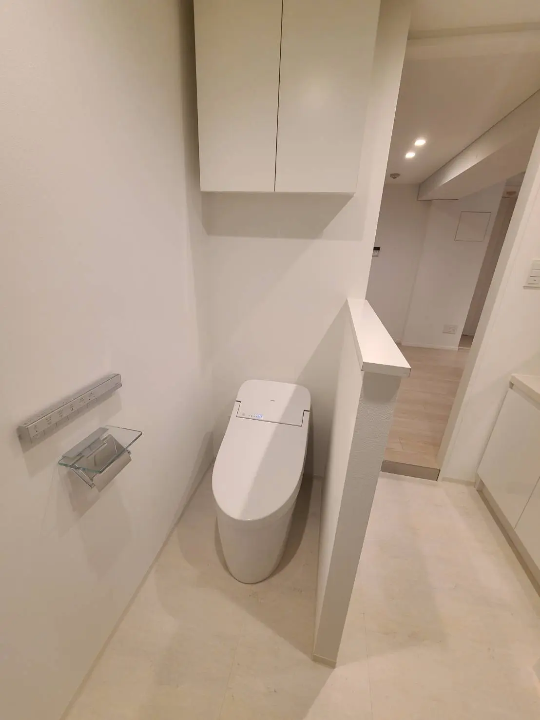 シンプルで清潔感のあるモダンなトイレ、壁掛けタイプのトイレットペーパーホルダーと手洗いカウンターが付いたインテリア