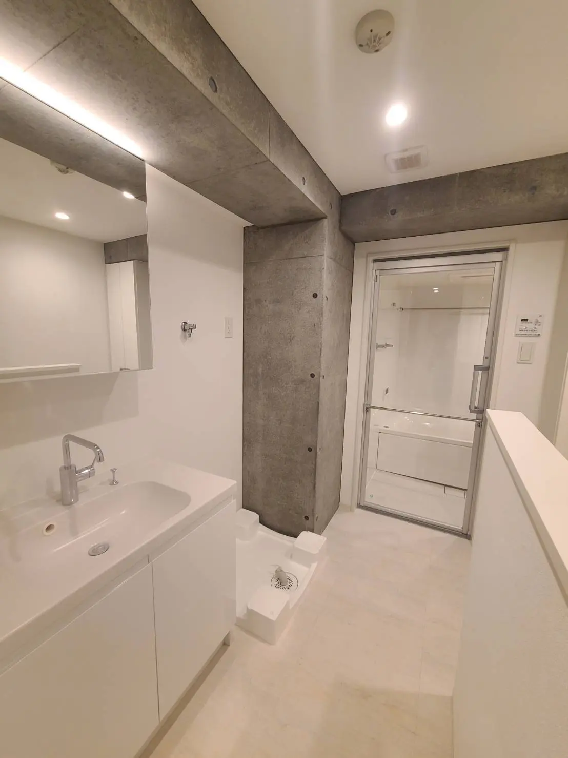 洗練されたデザインのモダンなバスルーム、コンクリートの壁、白い洗面台とトイレットペーパーホルダー、ガラス製のシャワールーム