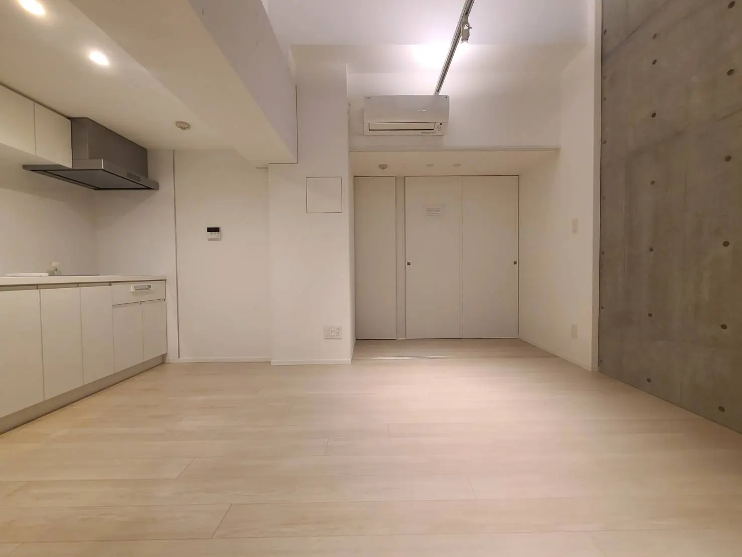 シンプルでモダンなキッチン、木目調の床、白いキャビネット、コンクリート壁のデザインが特徴の部屋
