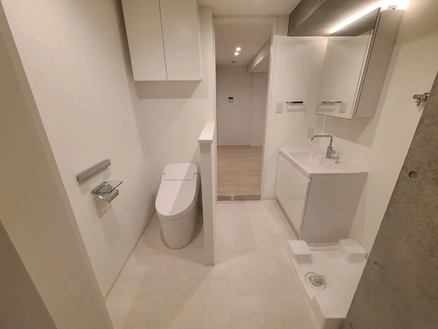 シンプルで清潔感のあるモダンなトイレ、壁付けのトイレットペーパーホルダーと洗面台、LED照明付きの鏡