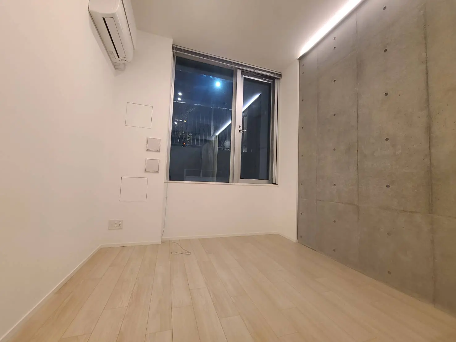 シンプルで洗練されたデザインの空の部屋、コンクリートの壁と木製フローリング、大きな窓からの都市の夜景