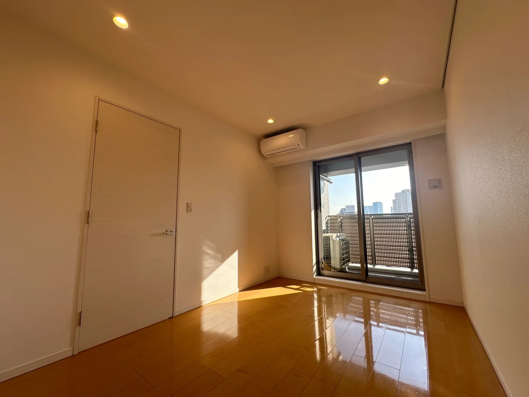 明るい日差しが差し込む都市の景色が見えるモダンなリビングルーム、光沢のある木製フローリングとスライド式バルコニードア