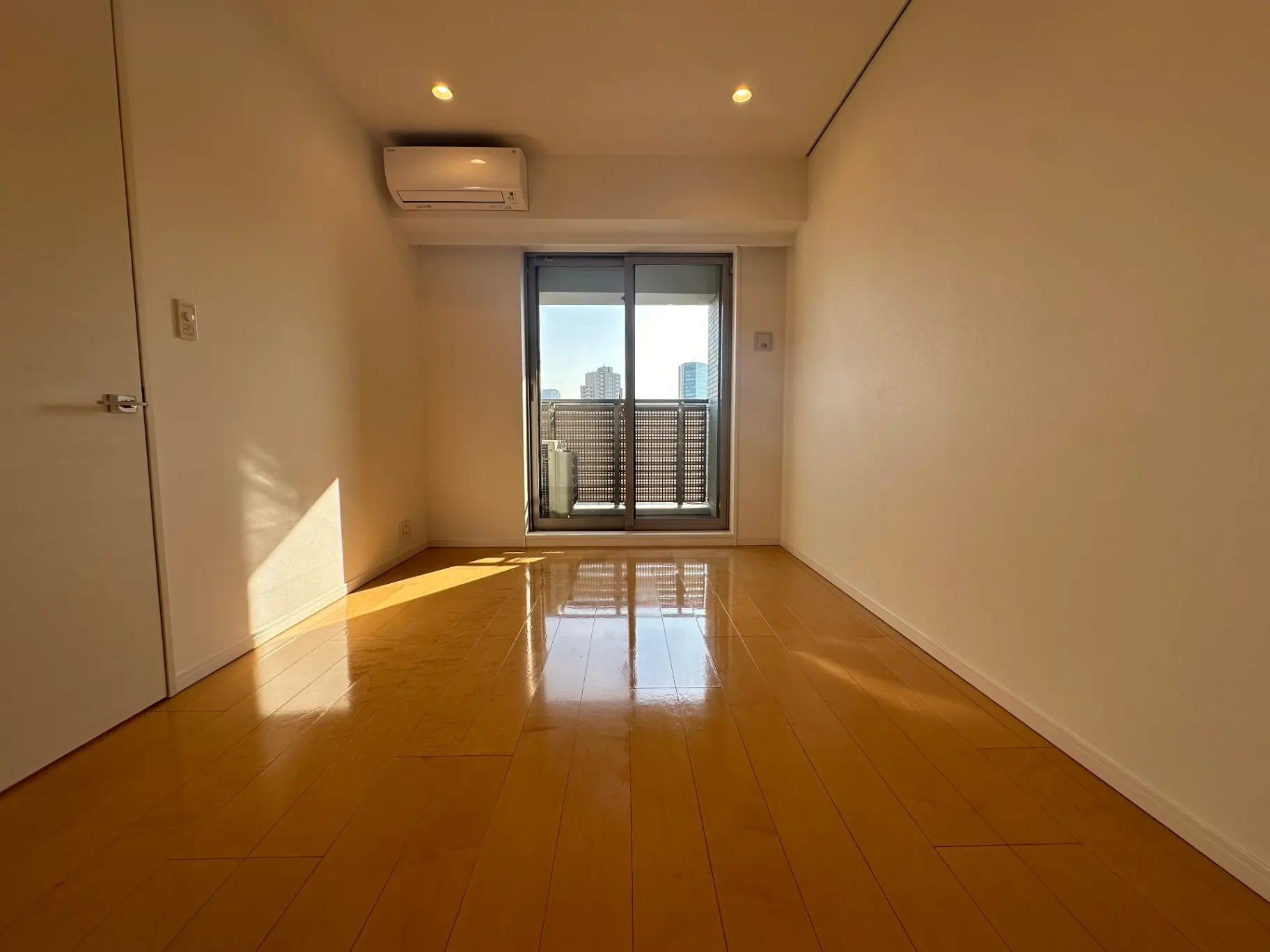 明るい日差しが差し込む広々とした空の部屋、ベランダ付き、クリーム色の壁と光沢のある木製フローリング