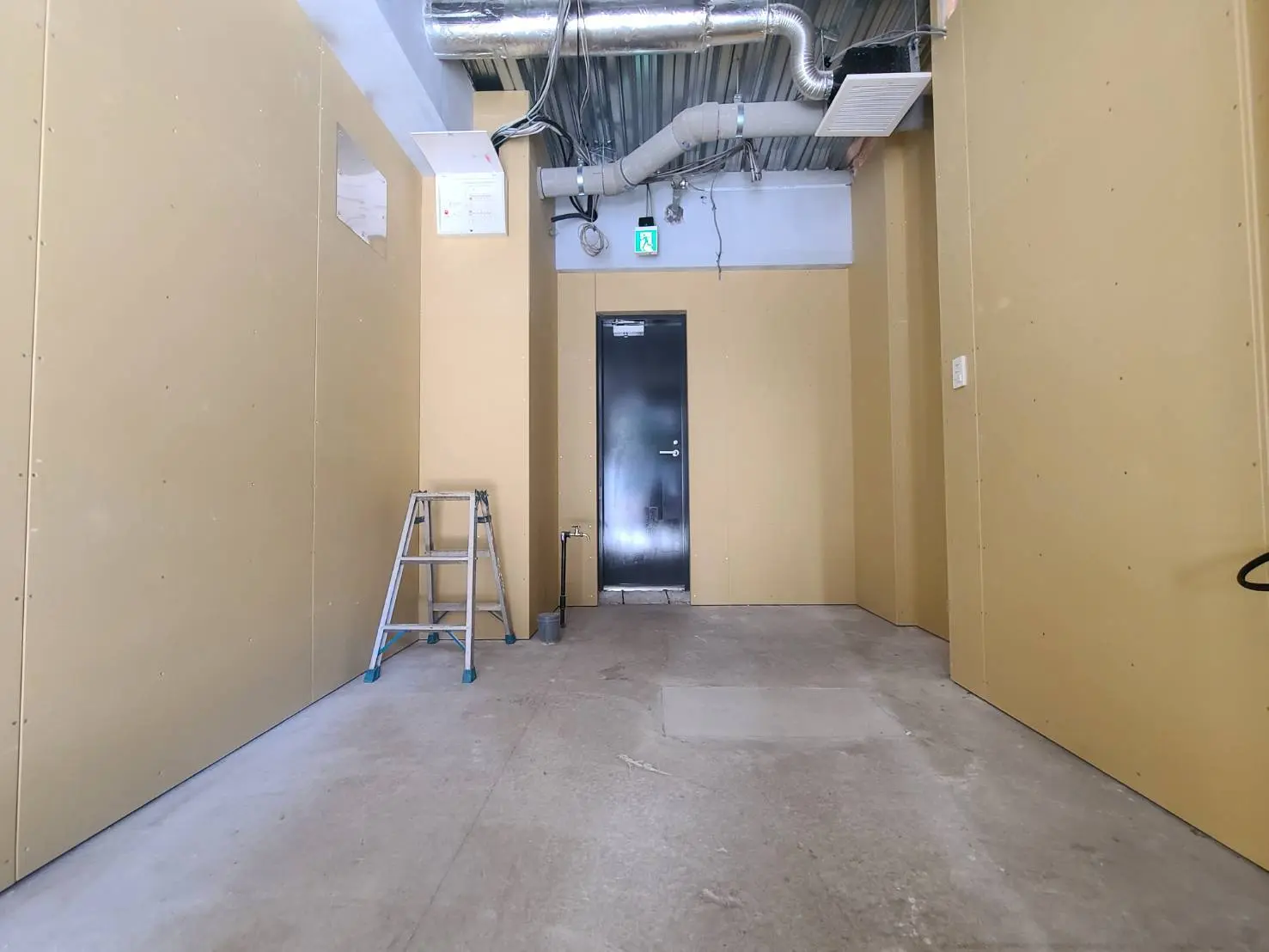 建設現場の内装作業中、黄色い壁とコンクリートの床、出口扉と脚立がある空間