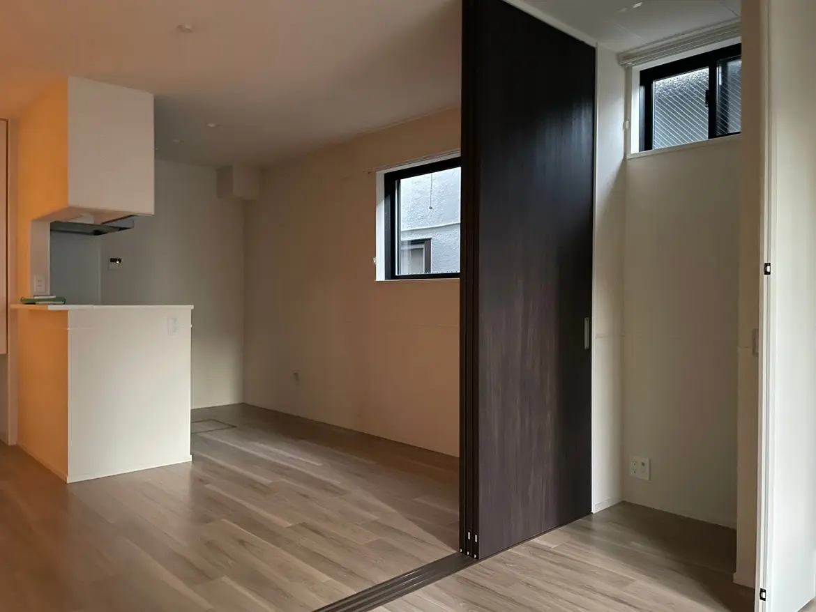 シンプルなデザインの新築マンションの一室、木目調フローリング、キッチンカウンターと採光窓があるリビングスペース