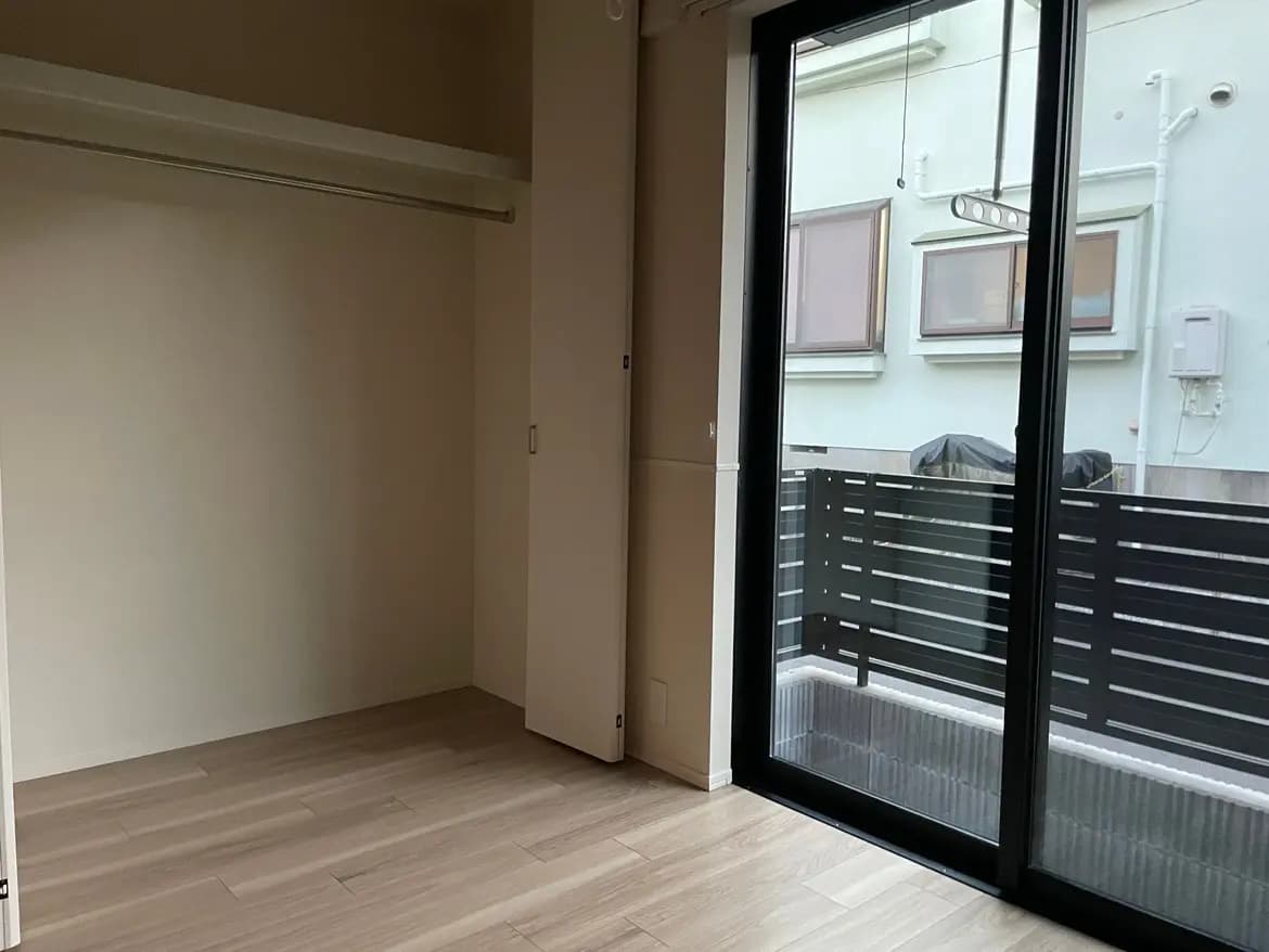 シンプルなデザインの空の部屋、木目調フロア、大きなガラス扉のバルコニーが特徴のインテリア