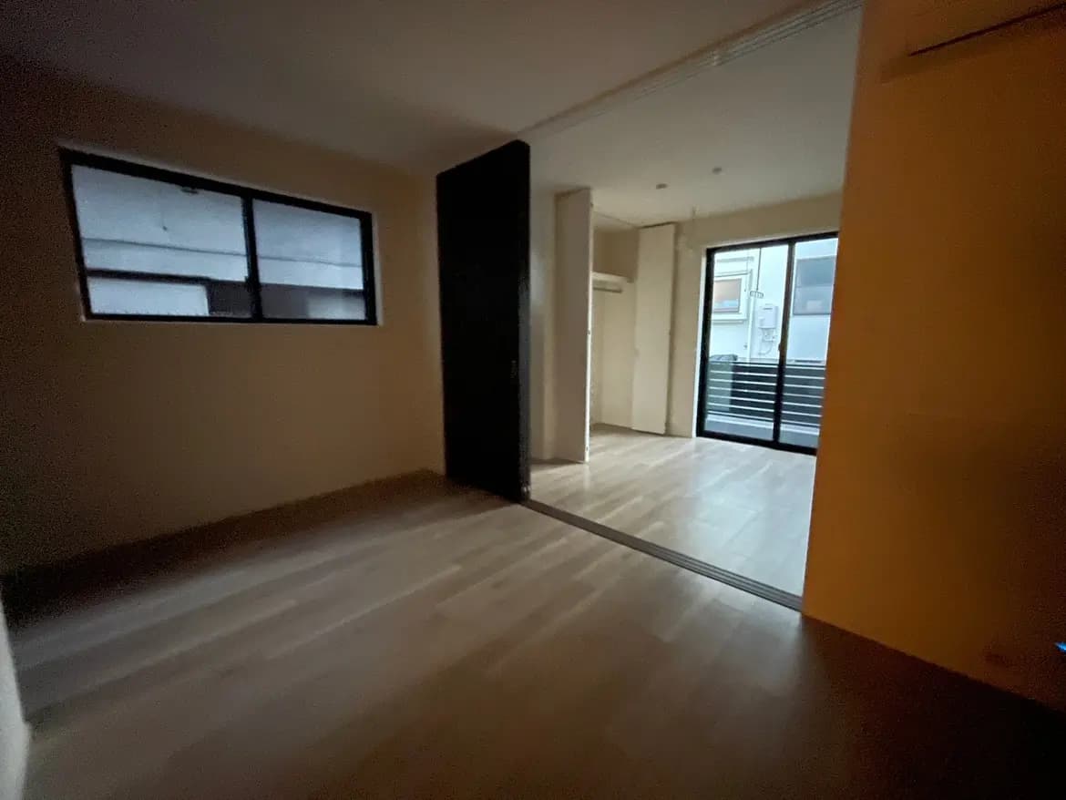 暗がりの部屋と明るいバルコニーへの出入り口、木製フローリング、和の要素を感じさせる窓デザイン