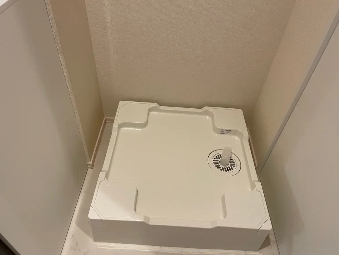 角部屋に置かれた白い浴室乾燥機、壁とタイルのディテールが見えるシンプルな内装