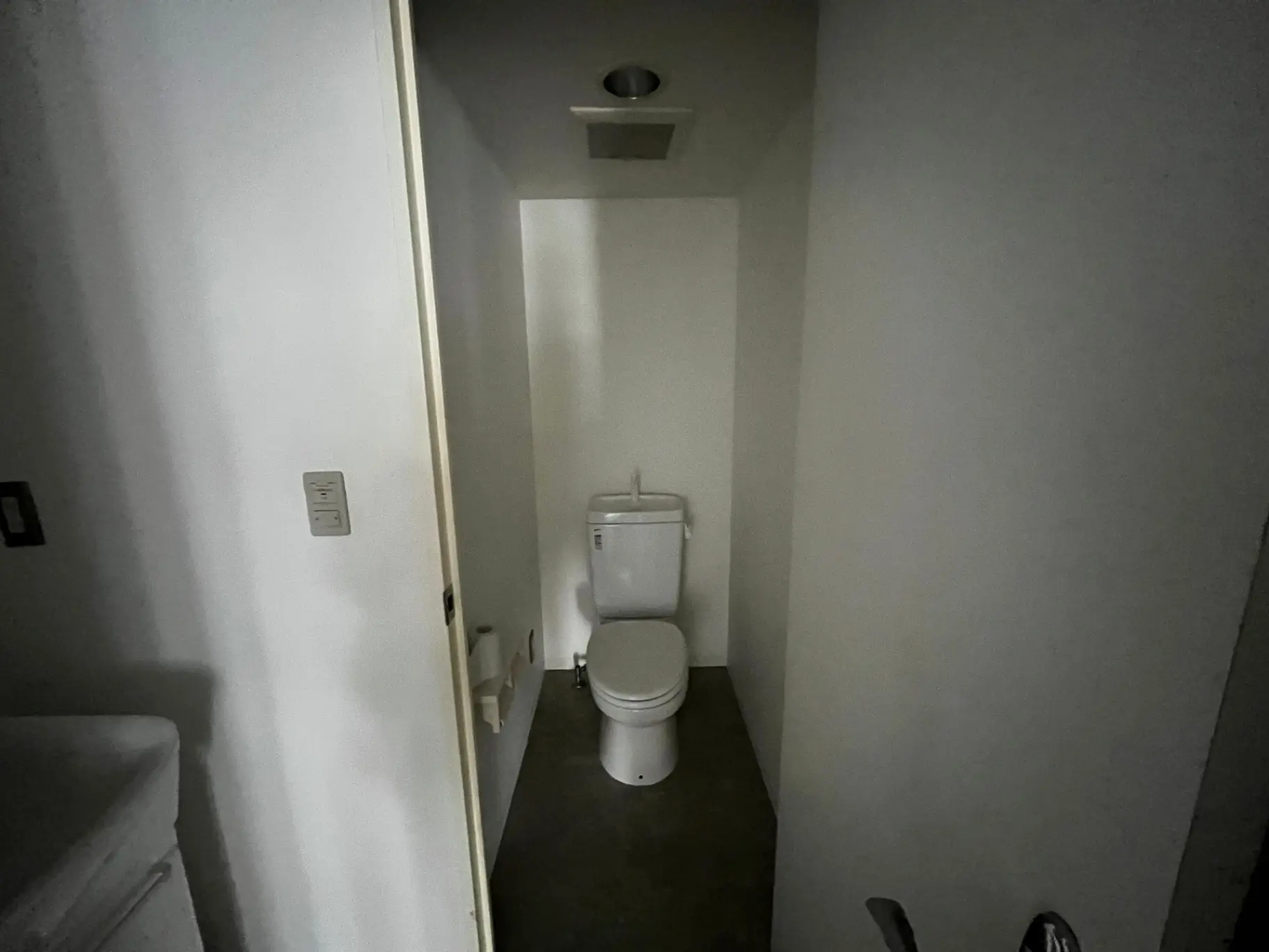 シンプルなデザインのトイレルーム、白い壁とタイル、暗い照明