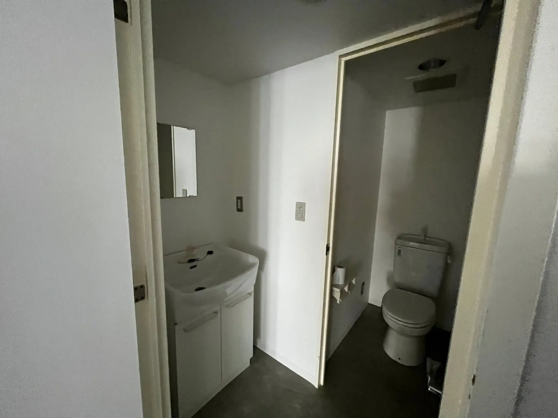 シンプルなデザインのトイレと洗面所、白い壁とフローリング、鏡付きの小さめの洗面台のインテリア