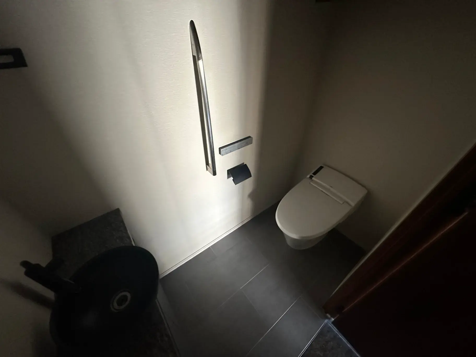 シンプルなデザインのトイレルーム、ダークグレーのフロアタイル、壁に取り付けられたトイレットペーパーホルダー