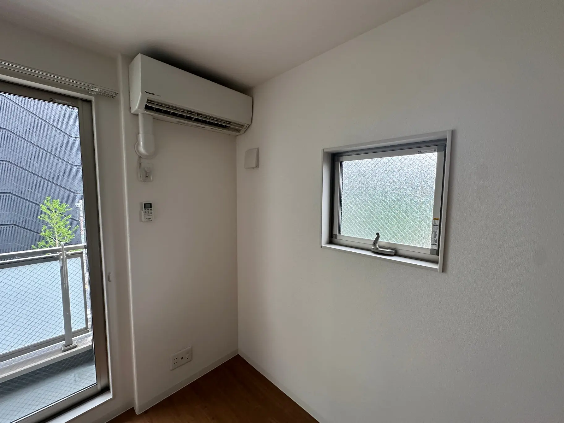シンプルなデザインの部屋、エアコンと小窓が付いた壁、床はダークブラウンのフローリング
