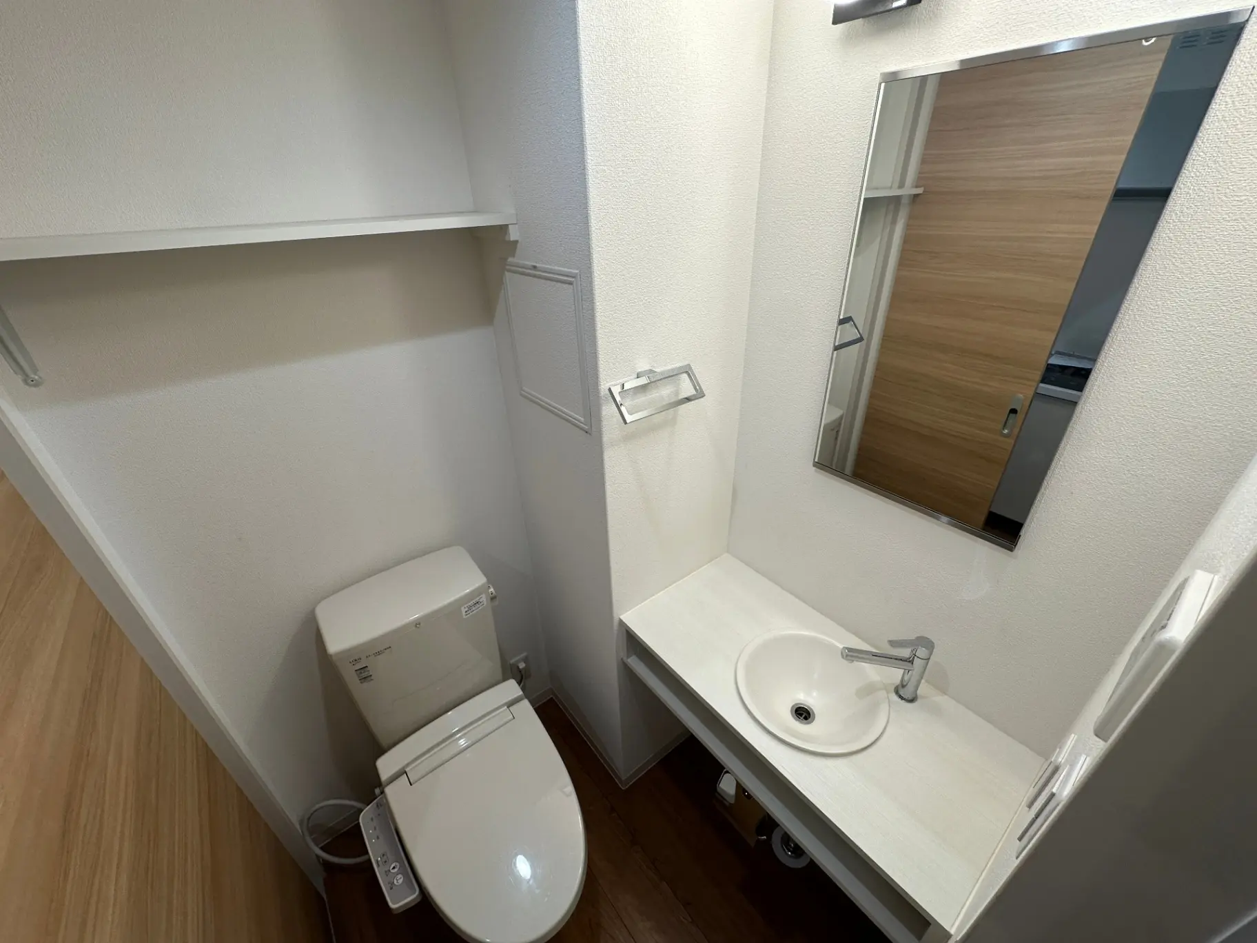 清潔感のあるホワイトカラーのトイレと洗面台、鏡付きの収納キャビネットと木目調のフローリング