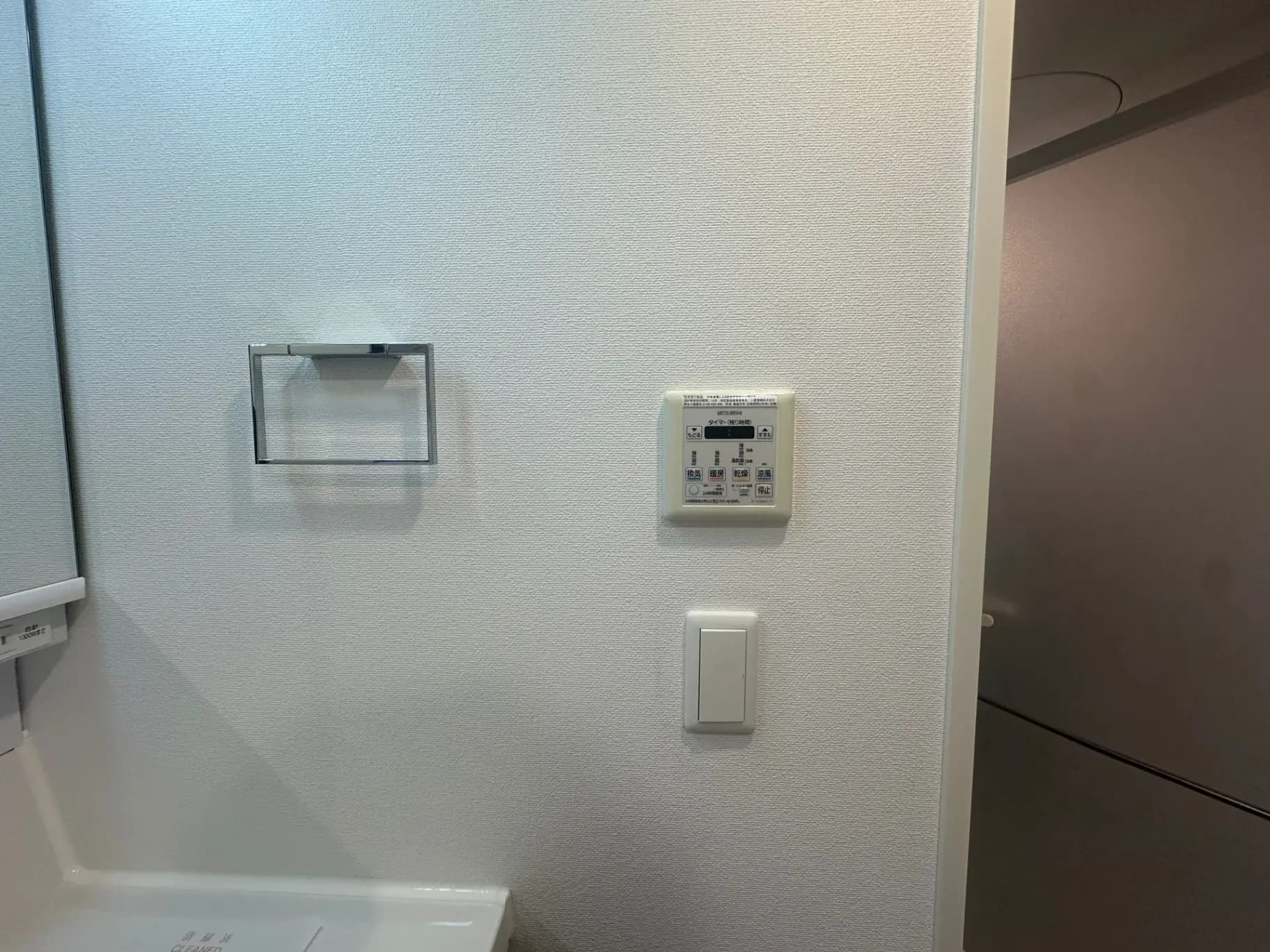 白い壁に取り付けられたエアコンリモコンと換気扇スイッチ、省エネルギー機能付きの住宅設備