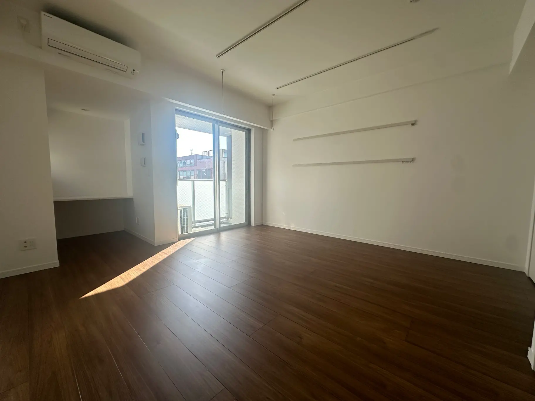 明るく広々とした空の部屋、ダークブラウンの床材、大きな窓から日差しが差し込むリビングルーム