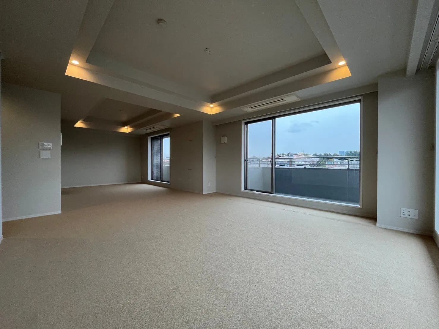 広々とした新築マンションのリビングルーム、埋め込み式照明と大きな窓、クリーム色のカーペットフロア