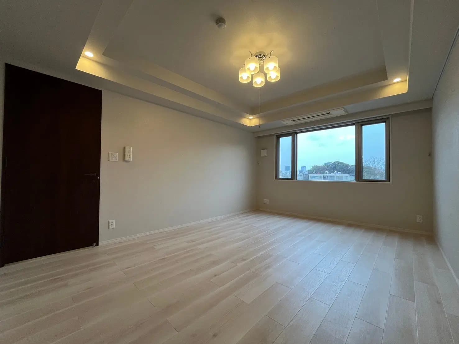 無垢フローリングの新築マンションの空き部屋、天井の間接照明とシャンデリア、大きな窓と都市の景色