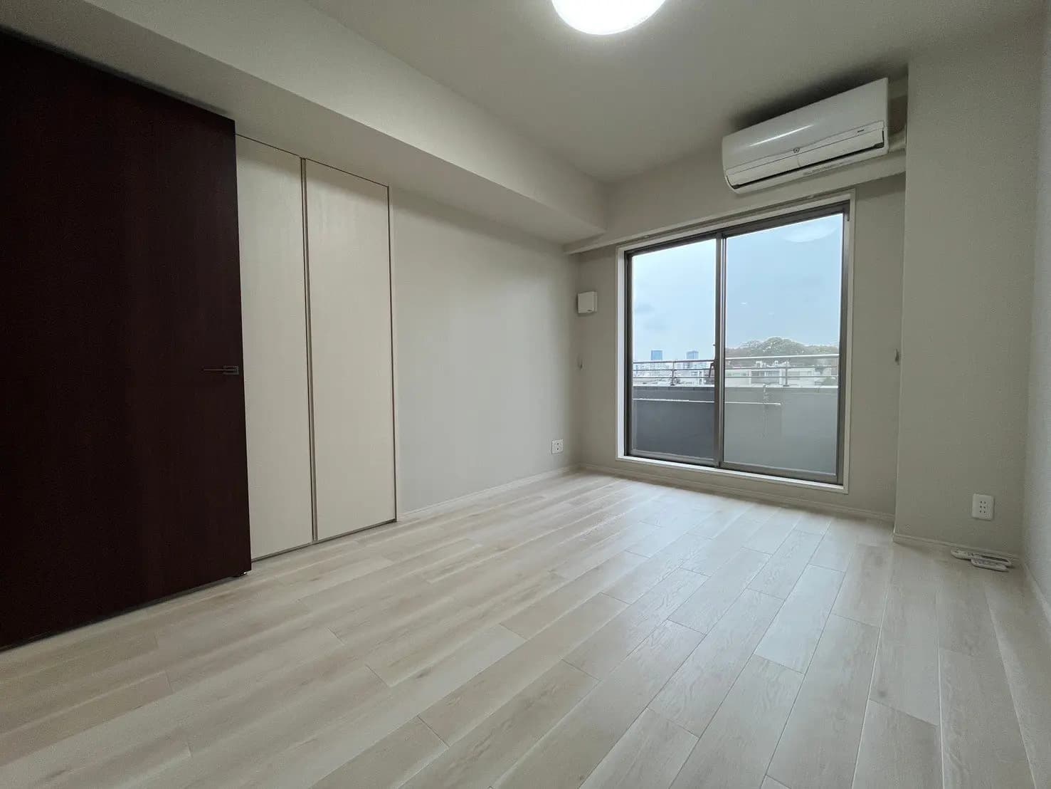 空間広々とした新築マンションの空の部屋、明るい木製フローリング、バルコニー付き大きな窓とエアコン