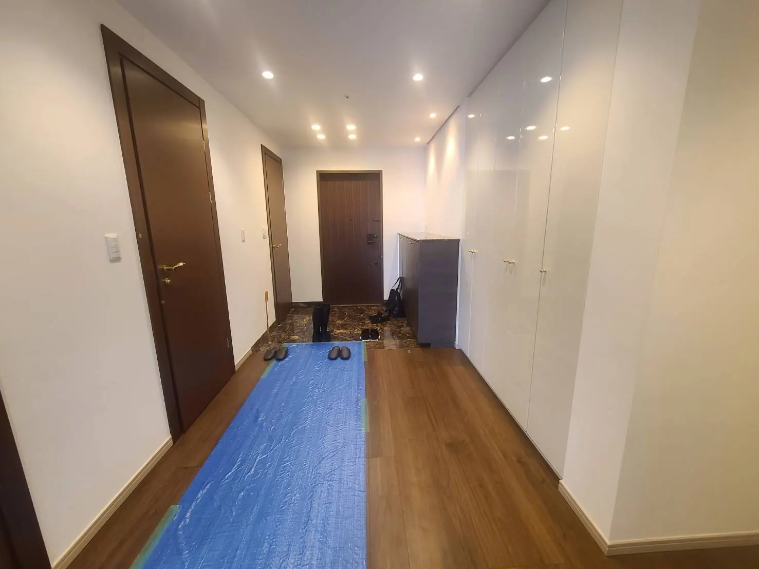 新築マンションの玄関ホール、木目調フローリング、白い壁面収納キャビネット