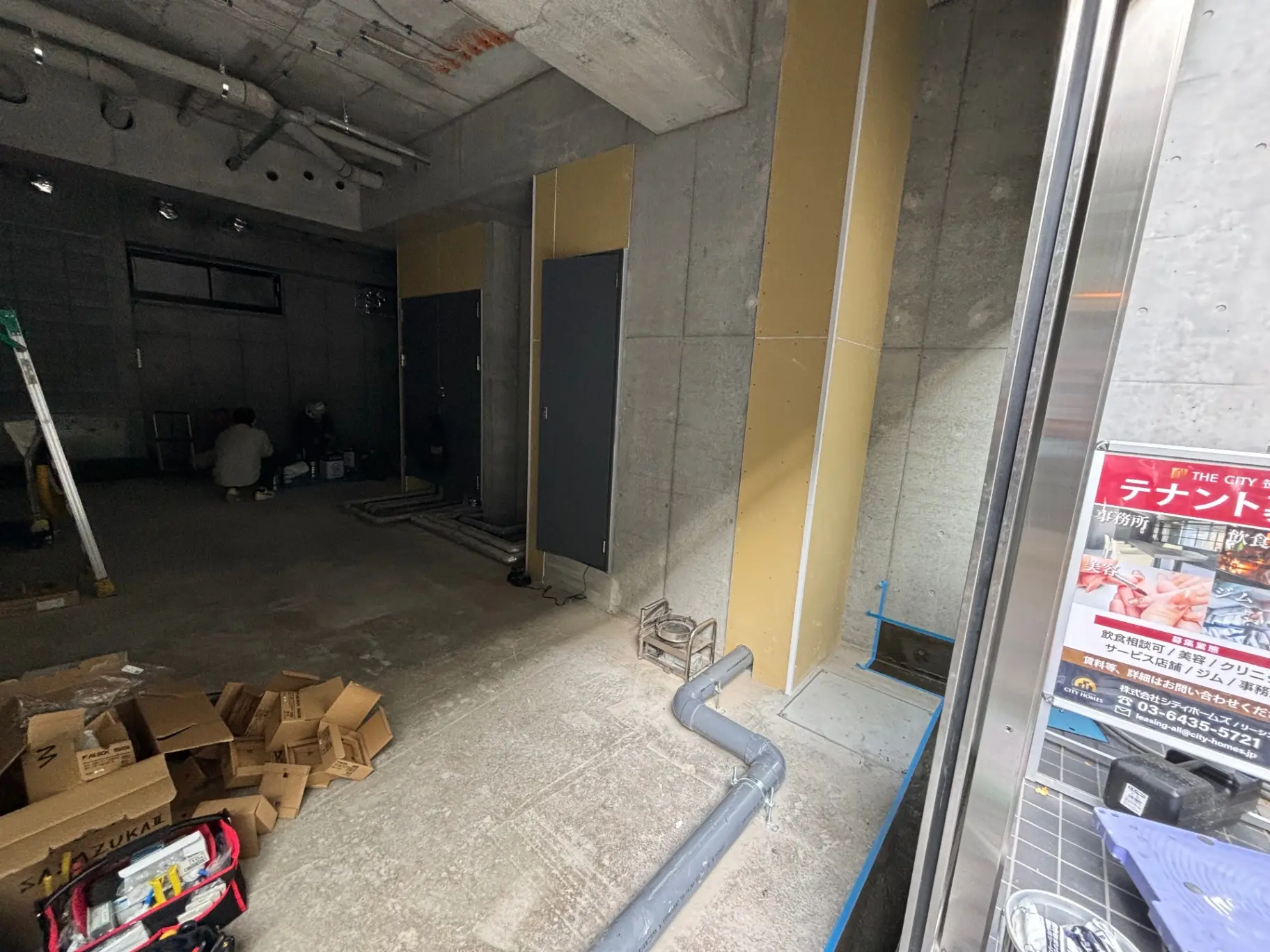 建設中の店舗の内部、未完成の壁と床、作業中の人物が見える工事現場