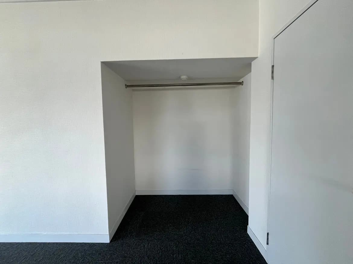 シンプルなデザインの空のクローゼットスペース、白壁に埋め込み型の収納棚とダークカラーのカーペット