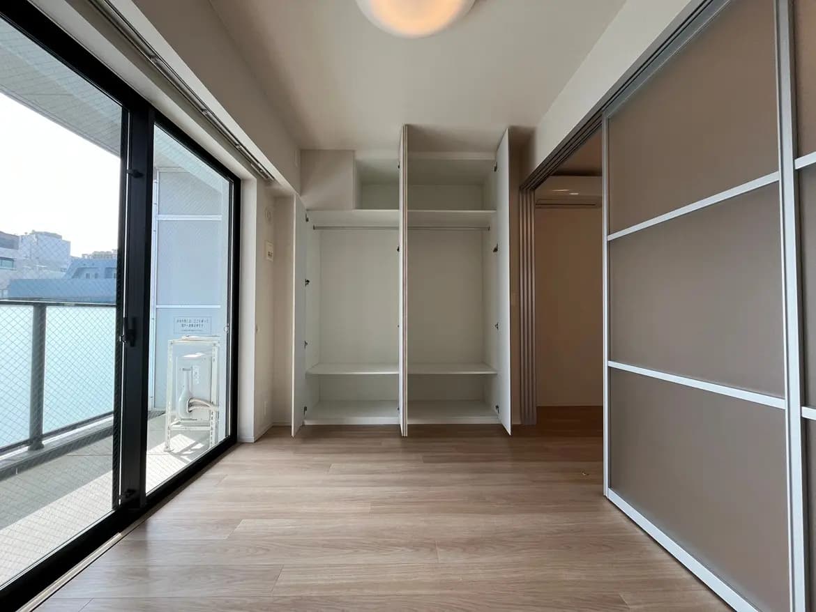 新築マンションの空の部屋、木目調フローリング、白い壁と建築されたクローゼット、大きな窓からの自然光
