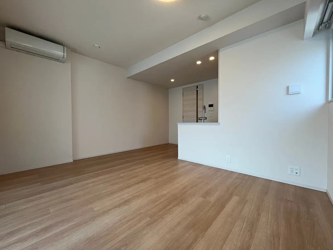 シンプルでスタイリッシュな新築マンションのリビングルーム、木目調フローリング、白い壁、内蔵照明とエアコン付きインテリア