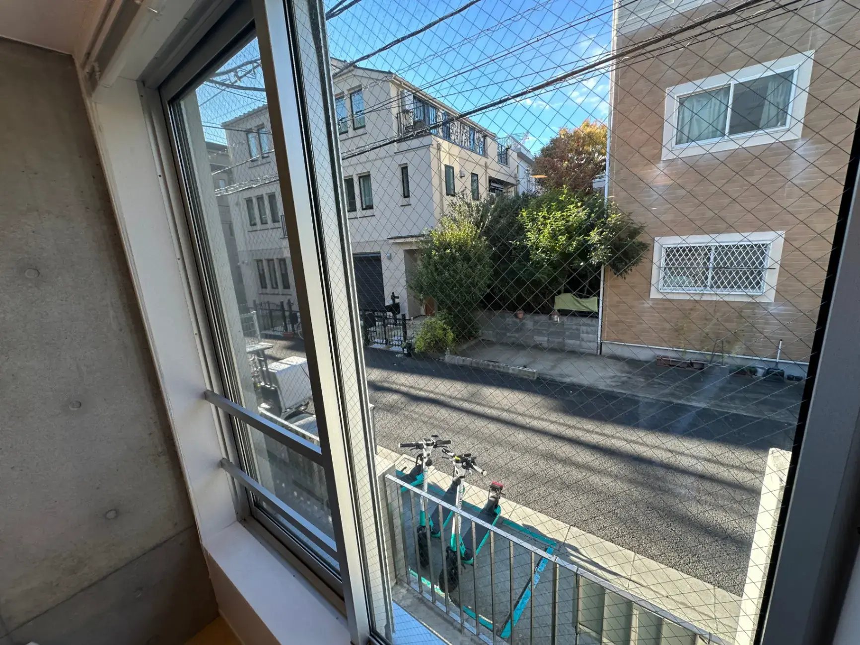 日当たりの良い窓から見える住宅街の風景、近隣の建物と緑の植物