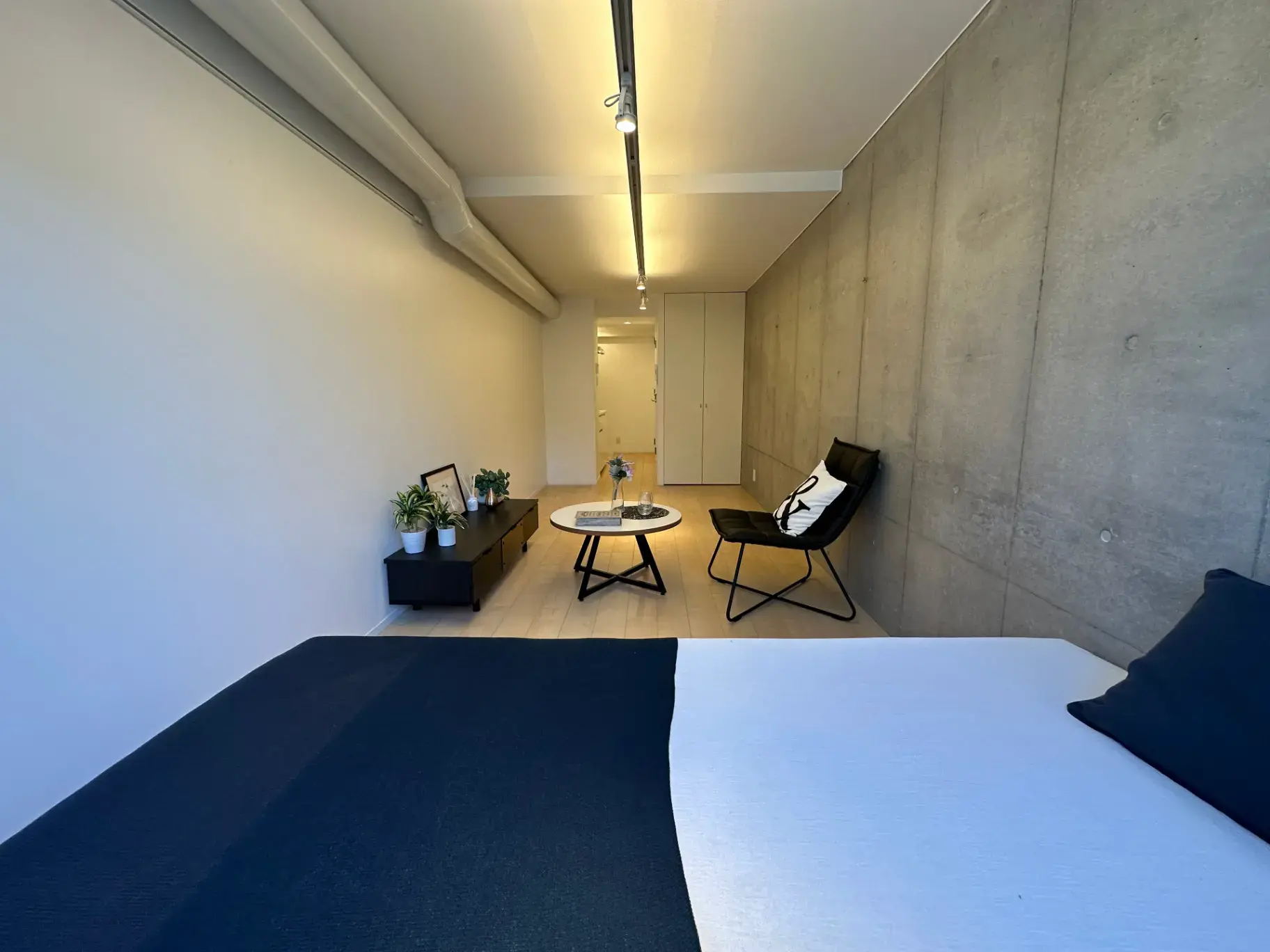 シンプルなコンクリートの壁とモダンなデザインの家具が特徴的な洗練されたベッドルーム、ナチュラルライトが差し込む明るい空間