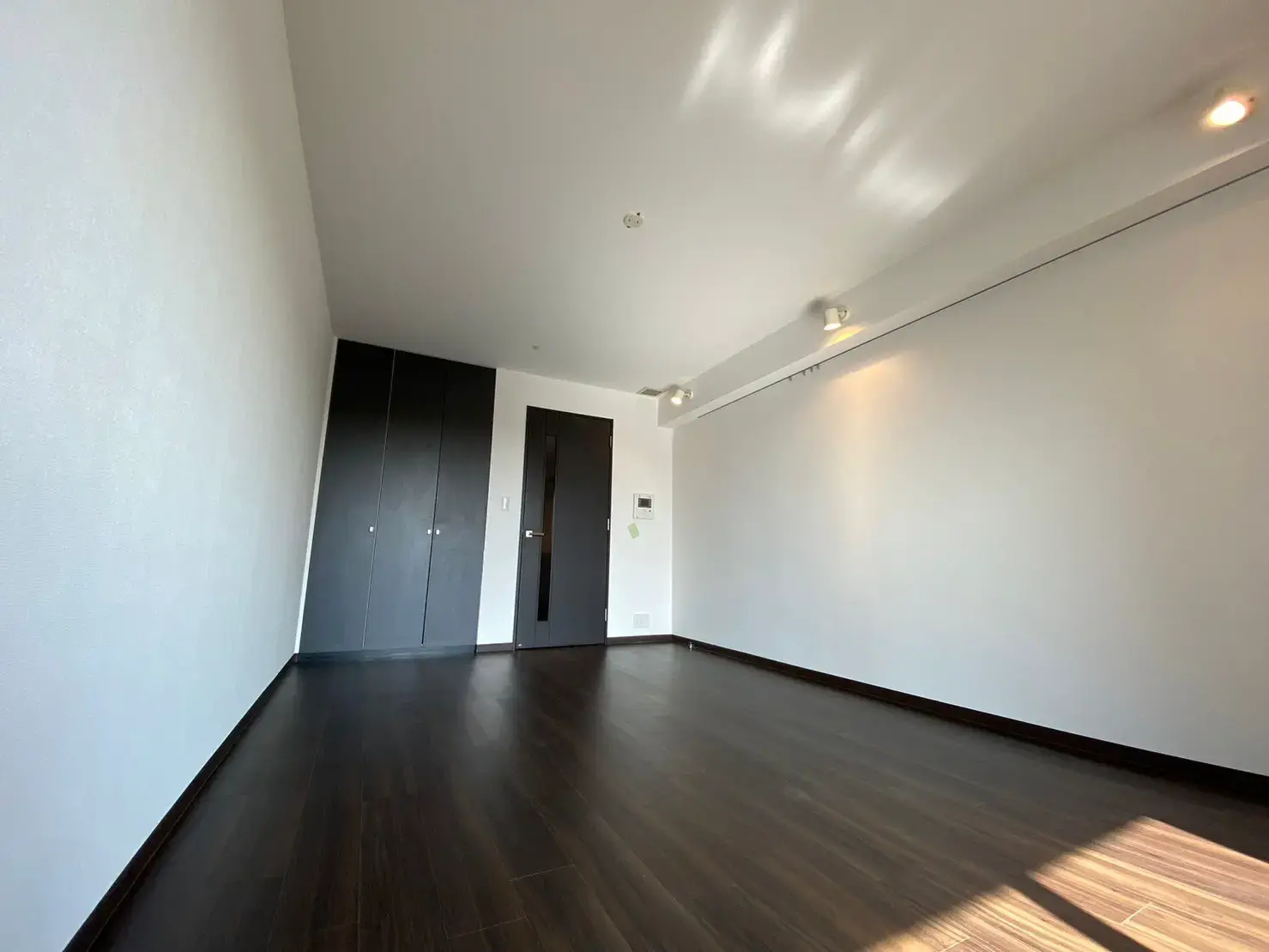 明るい日差しが入る無垢材フローリングの空の部屋と白い壁、スポットライトが付いたモダンな内装