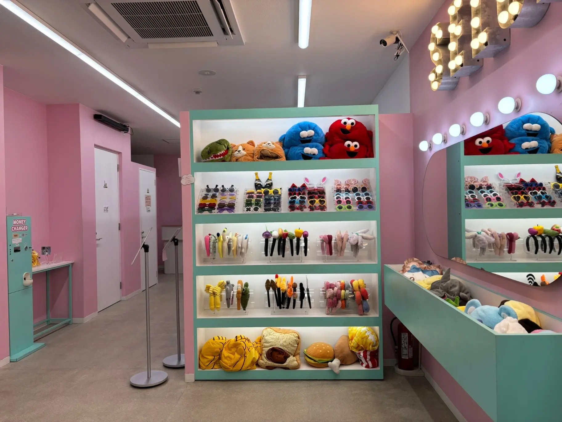 - 明るいピンクの壁に囲まれた店舗内、かわいいキャラクターのぬいぐるみやヘアアクセサリーが並ぶディスプレイと大きな鏡のあるインテリア