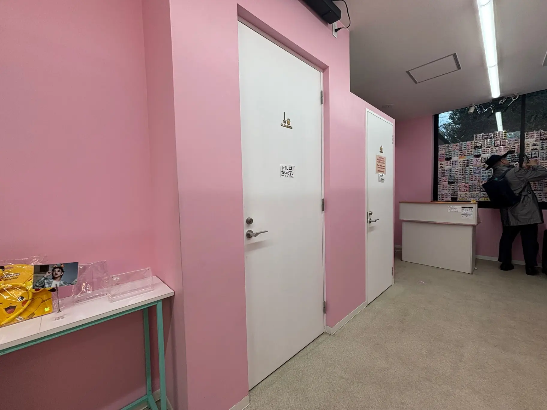 明るいピンクの壁に囲まれた待合室、白いドアと透明なテーブル、カウンターにおいてある展示物があるインテリア